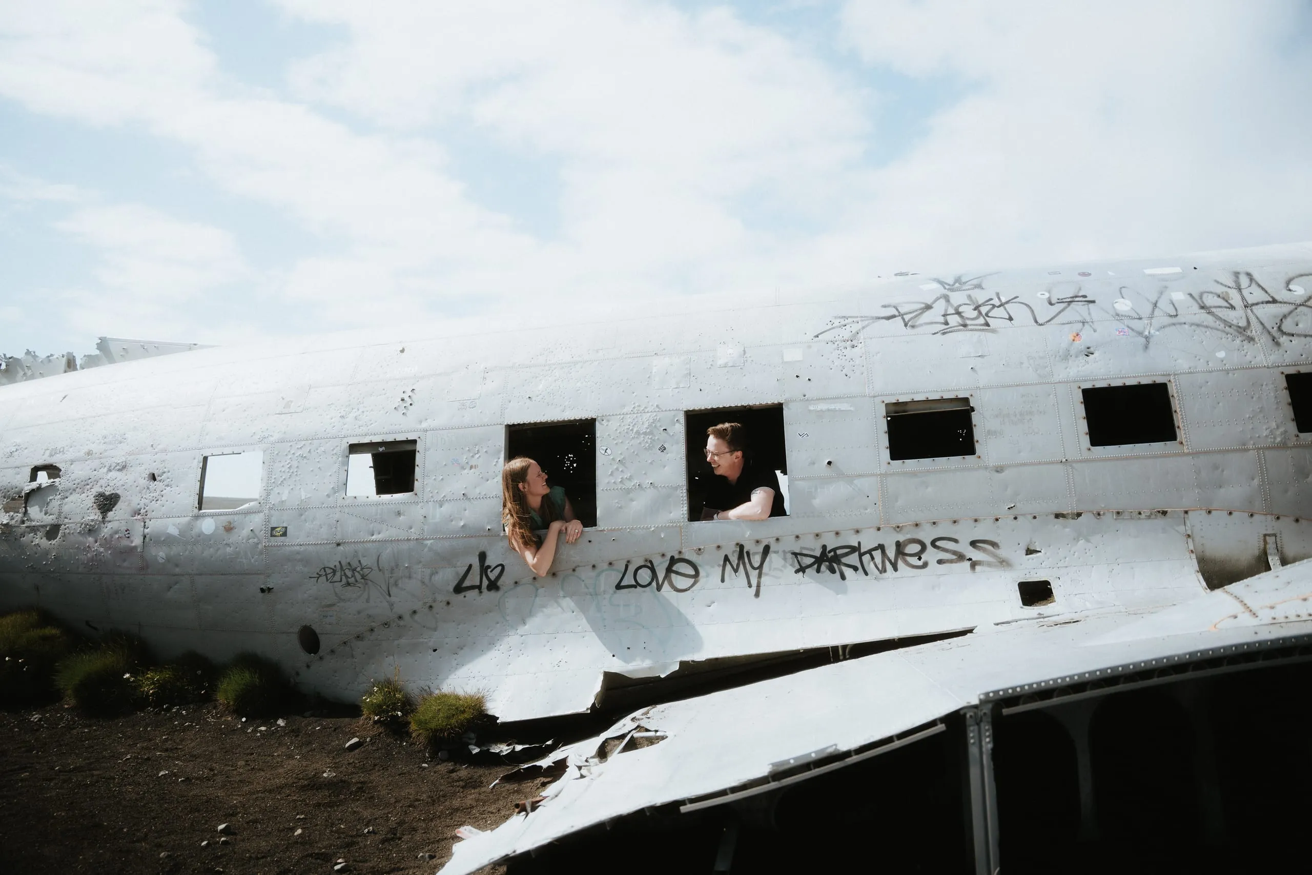 The couple smiling at each other from the windows of an abandoned airplane wreck
