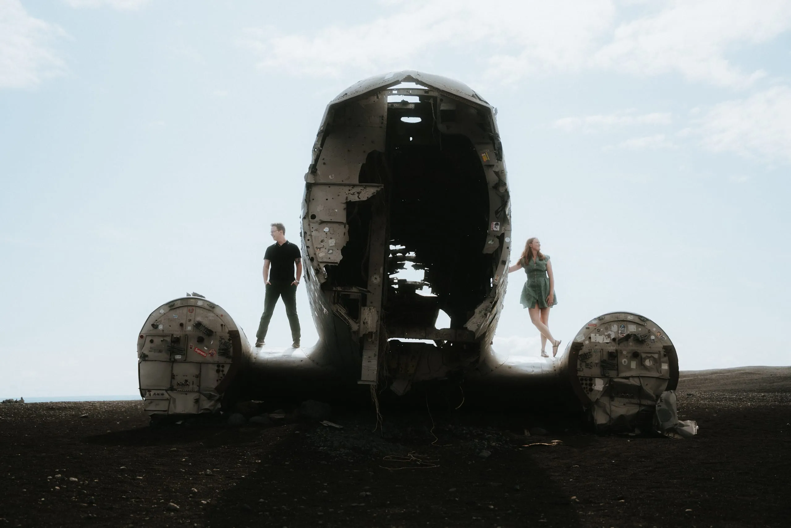 The couple standing on opposite wings of an abandoned plane under a pale sky