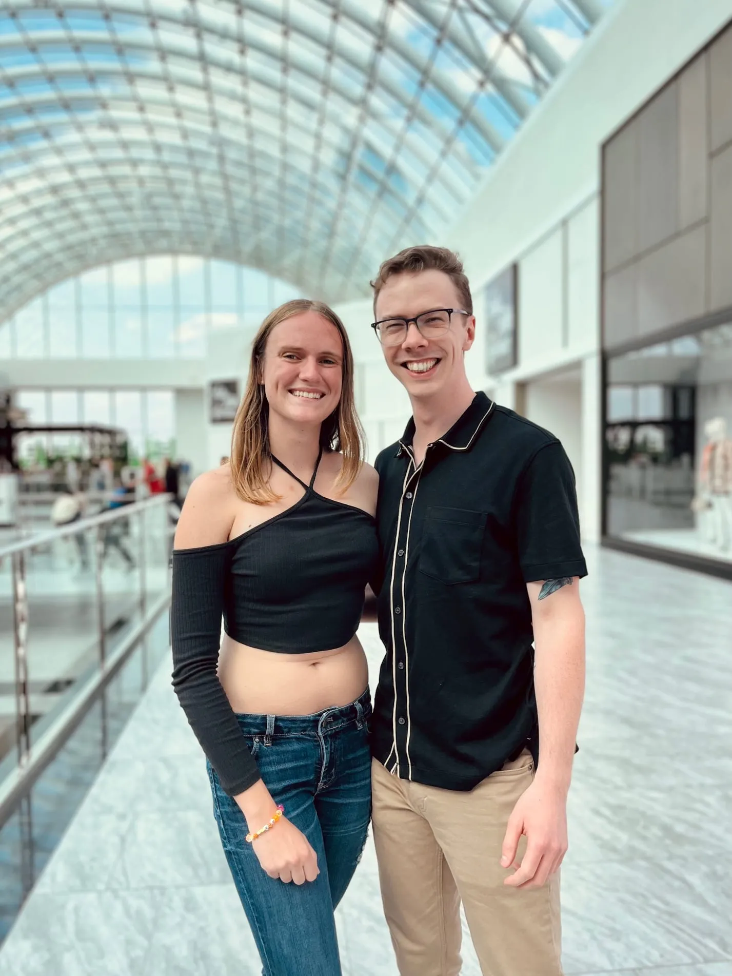 The couple smiling together under the glass roof of a bright atrium